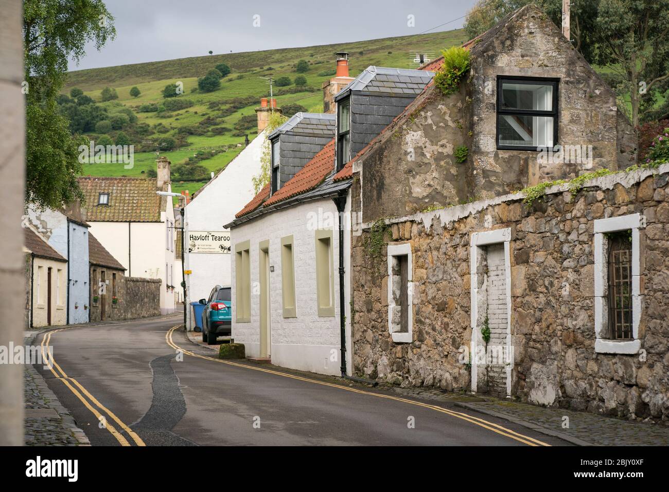 Strada asfaltata stretta tortuosa passato case in pietra nel piccolo villaggio medievale, Falkland, Fife, Scozia, Regno Unito, Europa Foto Stock