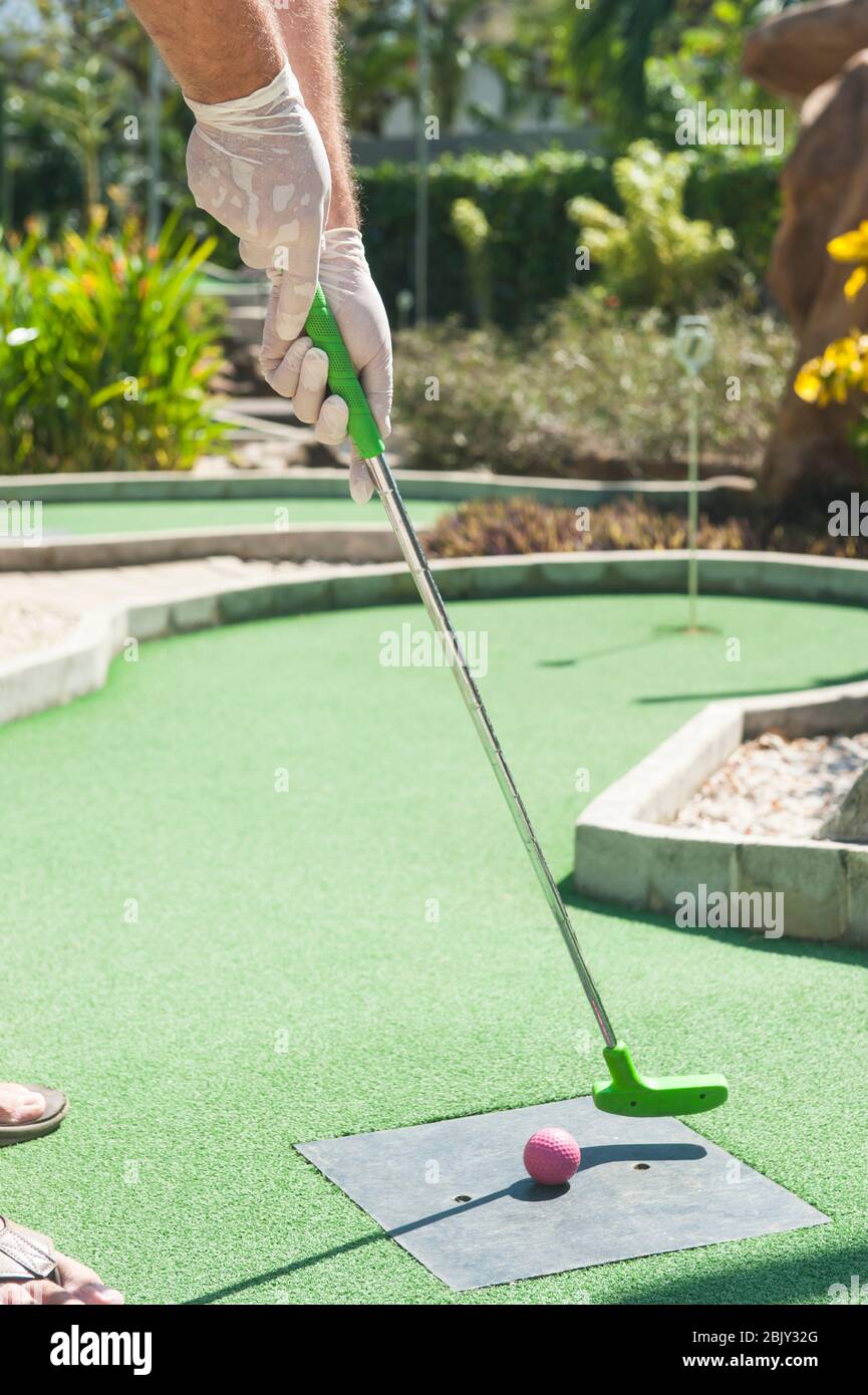 Uomo che si tea fuori al mini golf indossando guanti protettivi Foto Stock