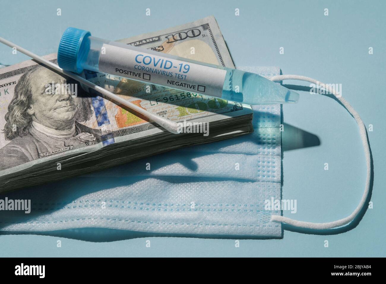 Fiala per analisi Covid-19 e tampone su una pila di 100 dollari bollette e maschera medica Foto Stock
