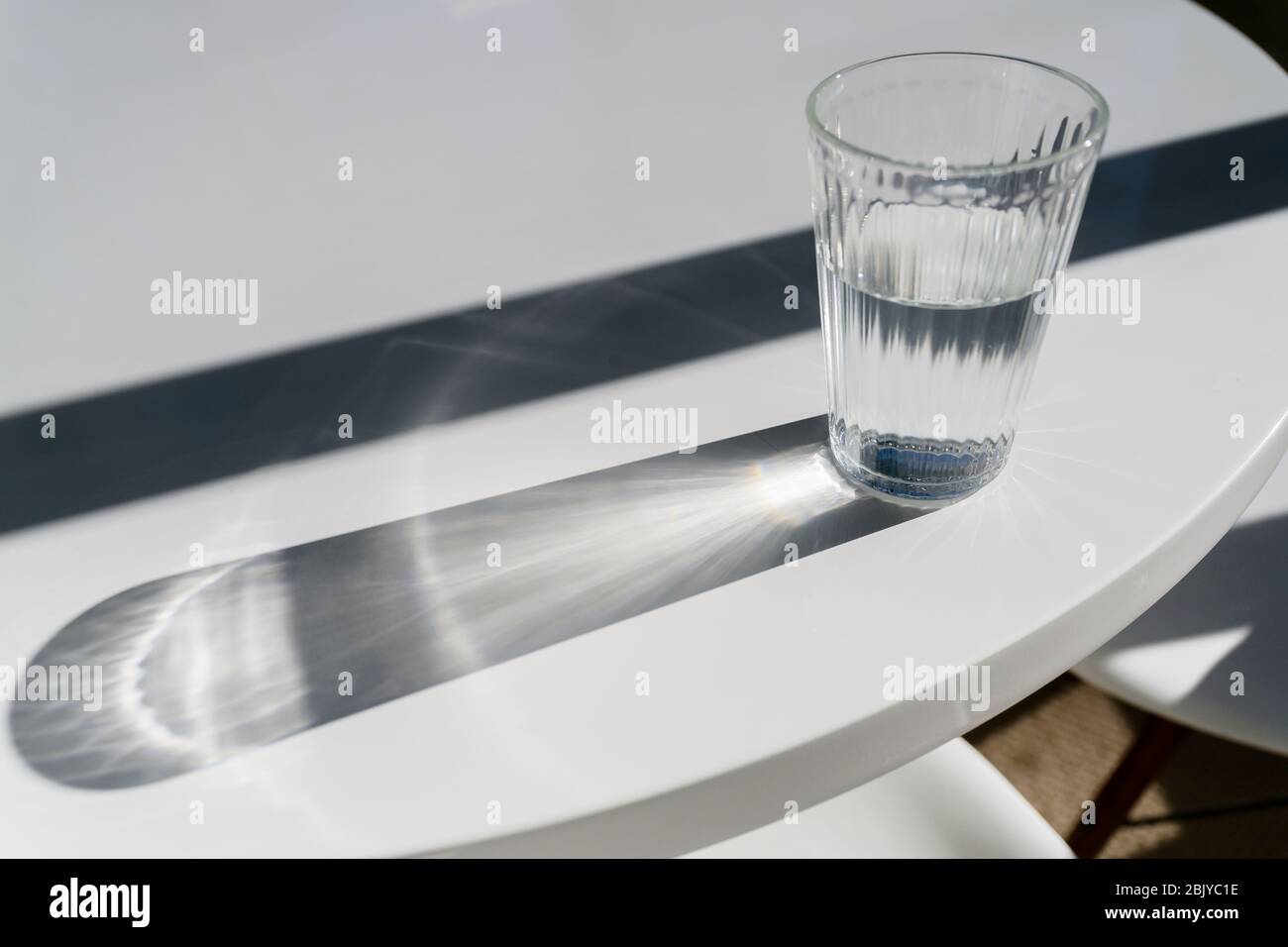Un bicchiere d'acqua sul tavolo che crea ombre Foto Stock