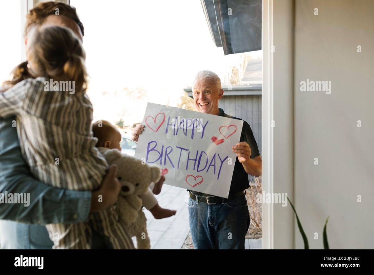 Nonno che mostra buon messaggio di compleanno alla famiglia con i nipoti (2-3 mesi, 2-3) attraverso la finestra Foto Stock