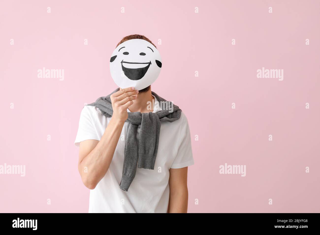 L'uomo faccia nascondere dietro il foglio di carta prelevato con emoticon sul colore di sfondo Foto Stock