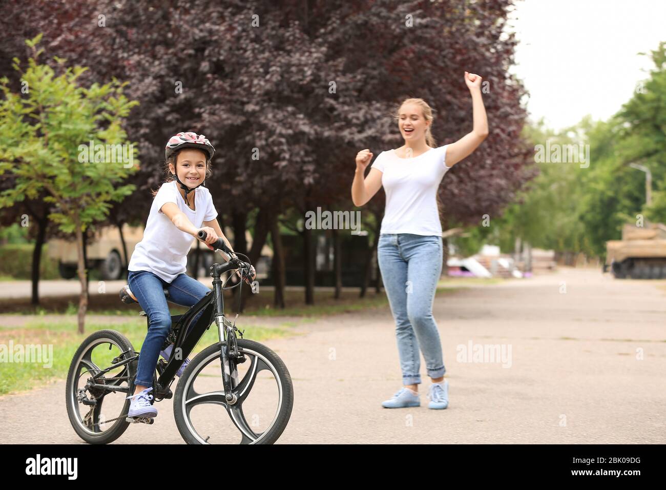 Madre orgogliosa di sua figlia che ha imparato a guidare la bicicletta all'aperto Foto Stock