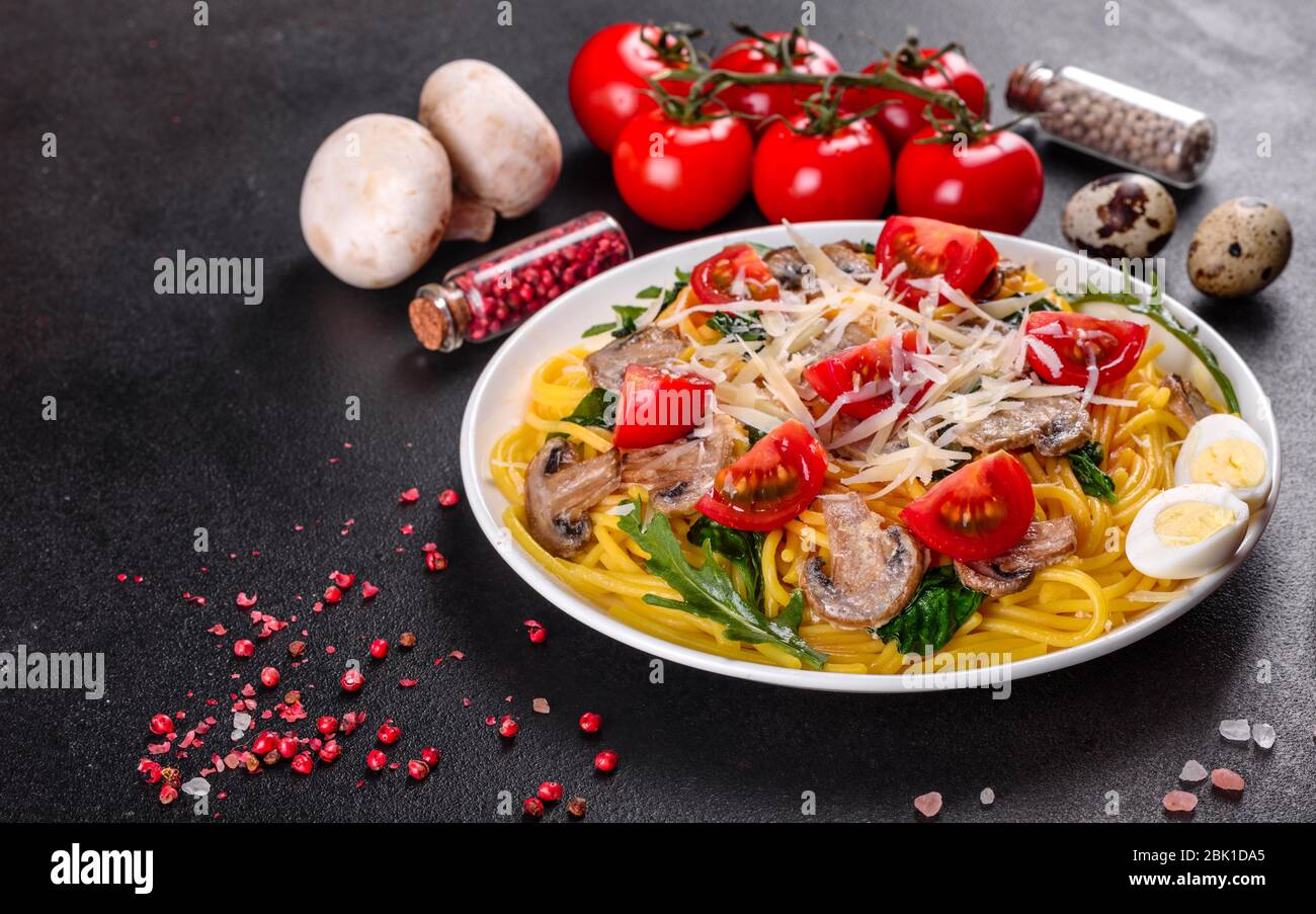 Spaghetti con funghi, formaggio, spinaci, rukkola e pomodori ciliegini. Piatti italiani, cultura mediterranea Foto Stock