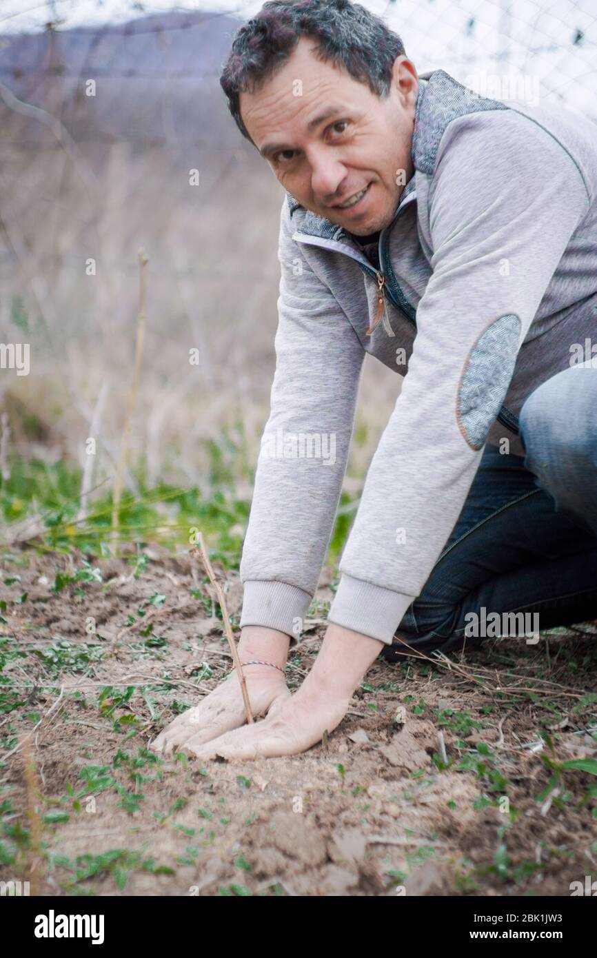 Uomo più anziano che pianta un albero in un campo in una giornata nuvolosa di primavera Foto Stock