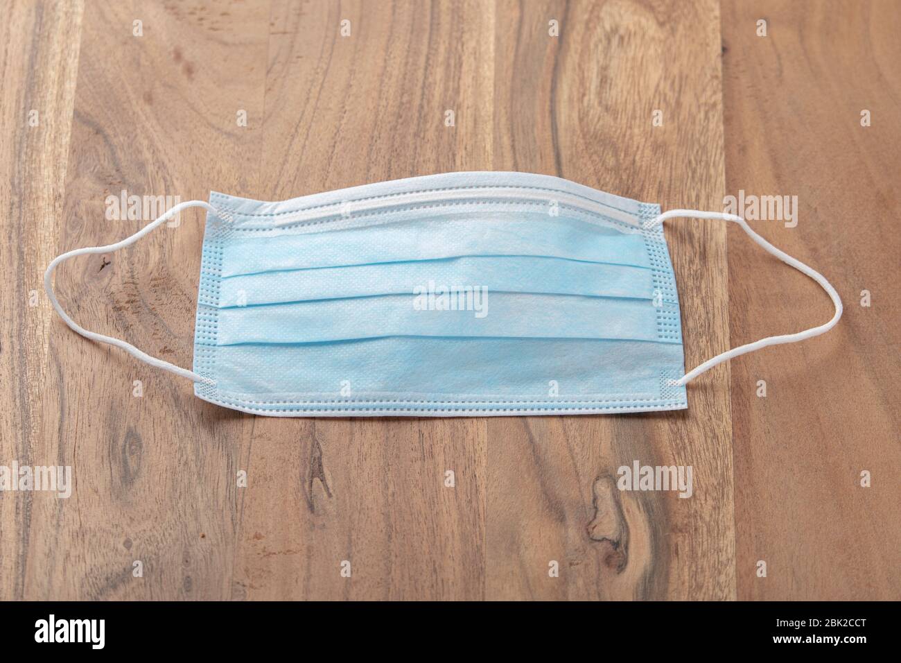 Foto di una maschera chirurgica blu posta su un tavolo di legno in rovere marrone massello. La maschera con il lato blu rivolto verso l'alto ed è pronta per l'uso. Foto Stock