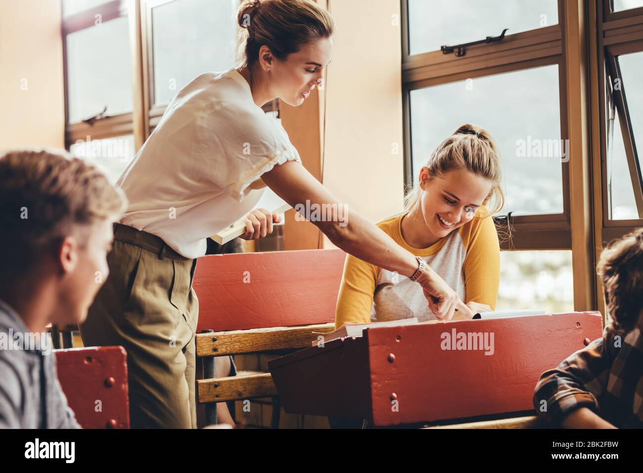 Insegnante di donne che assiste uno studente in classe durante la lezione. Professore femminile che aiuta una studentessa durante una classe a scuola superiore. Foto Stock