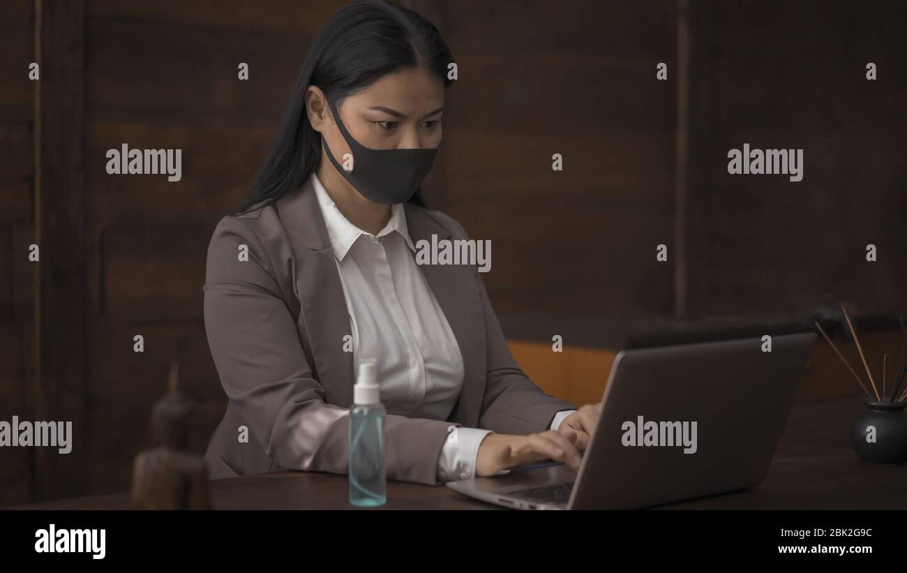 Donna asiatica in maschera che lavora su un notebook in ufficio Foto Stock