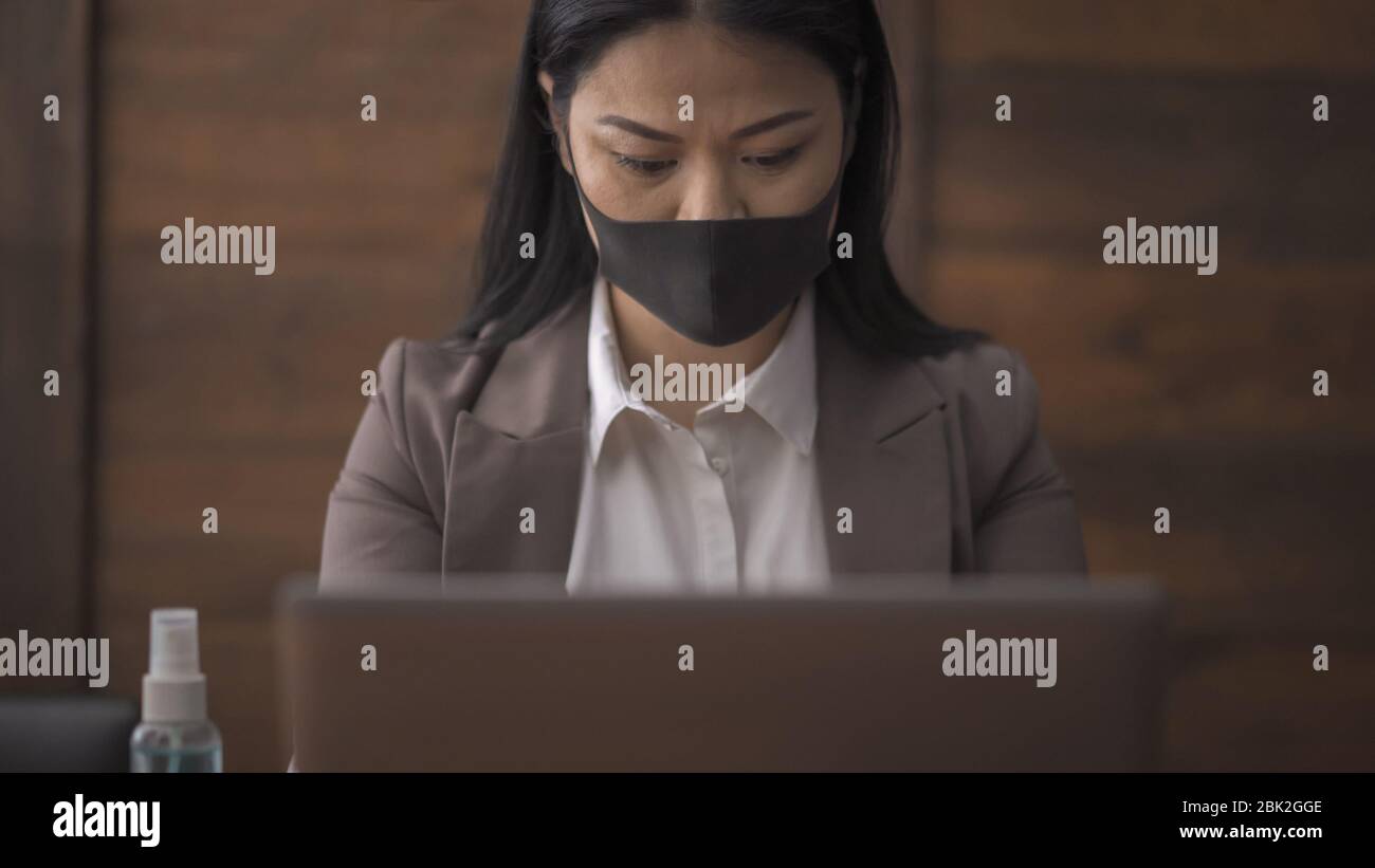 Donna d'affari asiatica che usa il computer che indossa la maschera medica Foto Stock