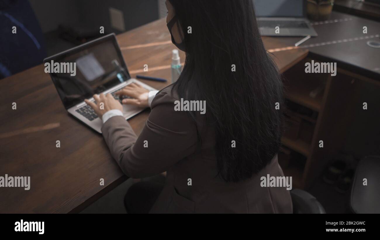 Vista posteriore di Brunette in maschere mediche su computer Foto Stock