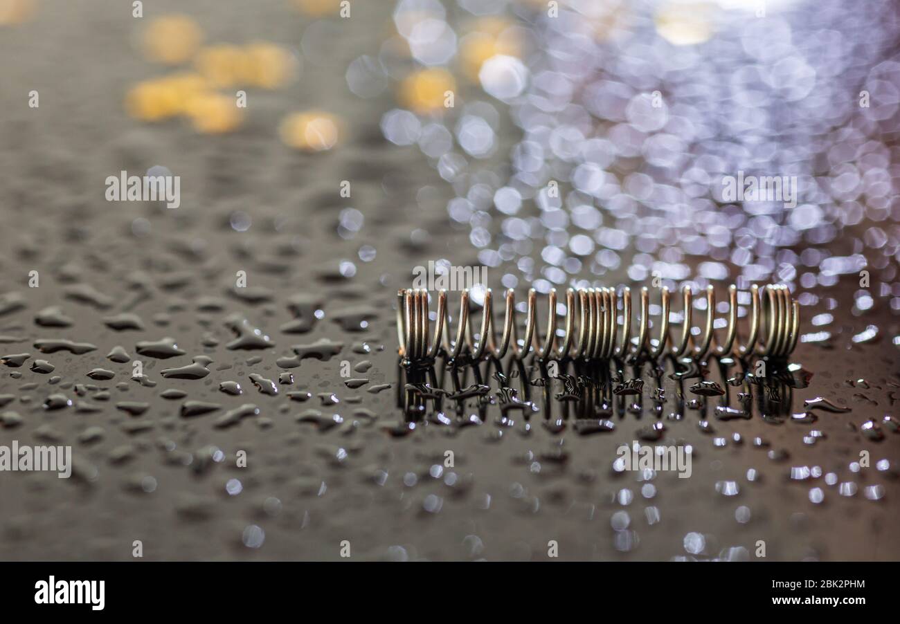 Molla metallica su sfondo nero. Meccanica di precisione. Piccoli oggetti. Parte della penna. Sfondo lucido. Muffa e gocce di acqua. Oro e argento. Foto Stock