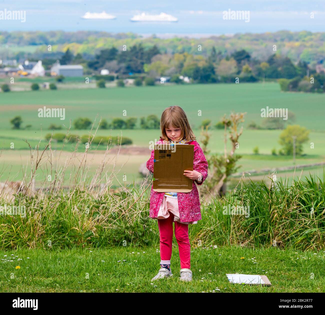 East Lothian, Scozia, Regno Unito. 1 maggio 2020. Scuola domestica: Alice, 5 anni è un allievo della scuola primaria 1. Lavora su un'attività di numeracy all'aperto alla strada imparando a contare, contando automobili, ciclisti, pedoni, trattori e camion con il paesaggio rurale e navi da crociera motballed nel Firth of Forth in lontananza Foto Stock