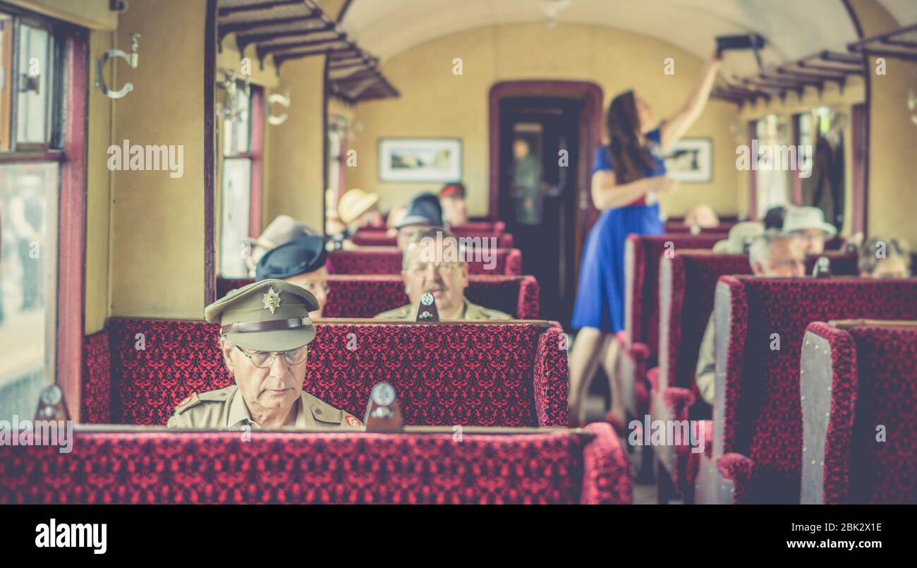 Retro, vista vintage dei passeggeri della ferrovia all'interno della carrozza ferroviaria britannica vintage, treno a vapore britannico, evento estivo in tempo di guerra degli anni '40. 1940 uomo in treno in uniforme. Foto Stock