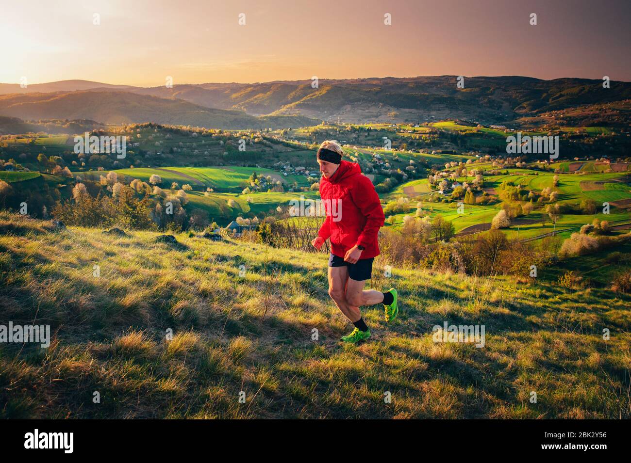 Allenamento dei runner maschi nella natura primaverile del mattino. Uomo che corre su collina. Splendido scenario primaverile sullo sfondo. Hrinova villaggio in Slovacchia Foto Stock