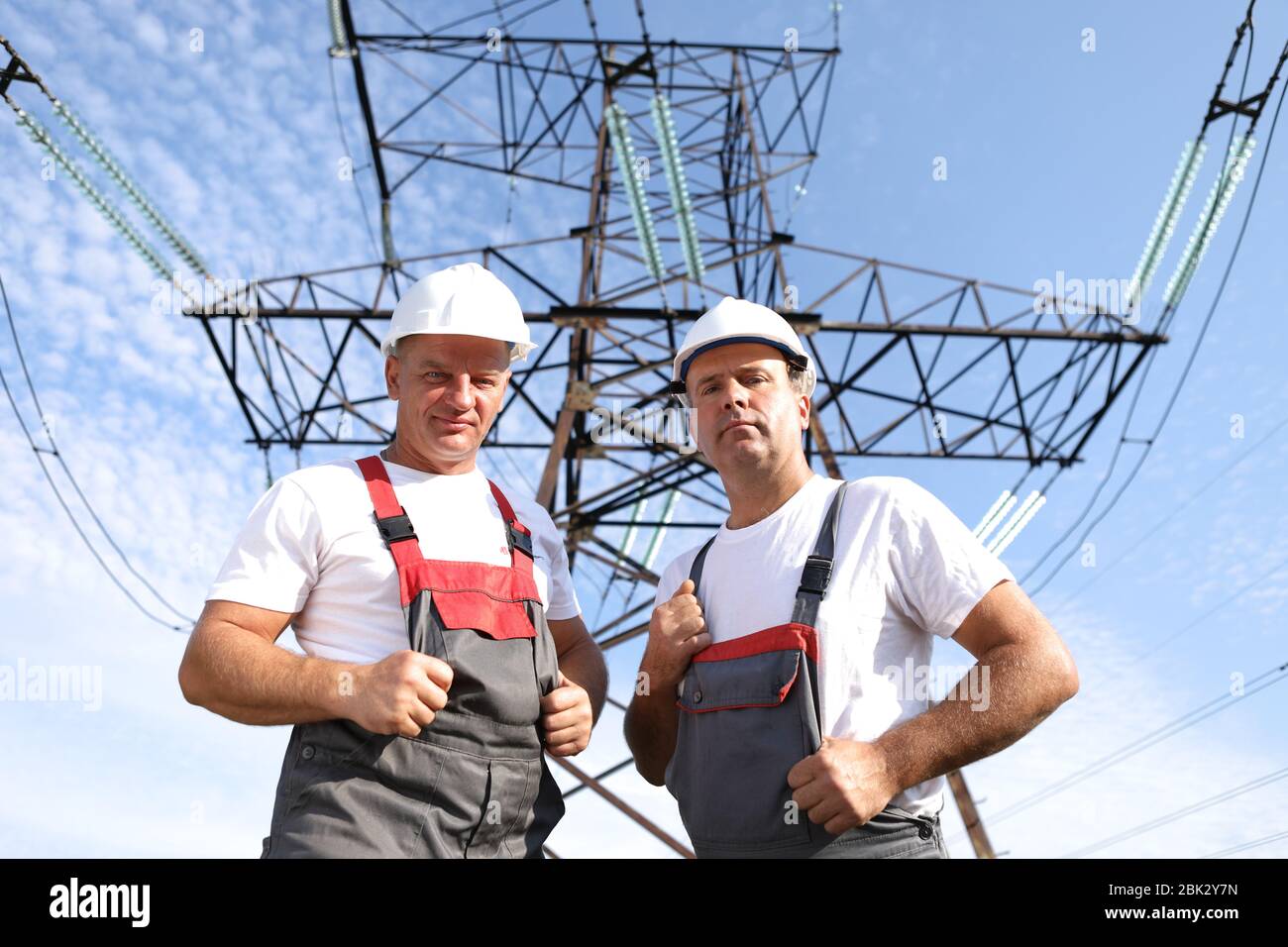 Due elettricisti maschi adulti mostrano come. Due lavoratori di centrali elettriche sullo sfondo di un pilone elettrico. Supporto elettrico 8000 kilowatt Foto Stock