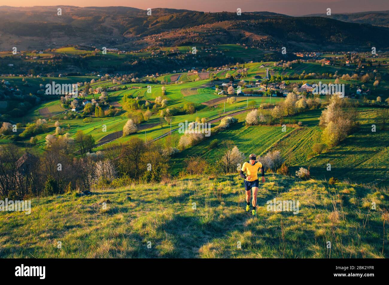 Percorso in bella natura primaverile, atleta maschile correre su collina, primavera mattina paesaggio in background, Foto Stock