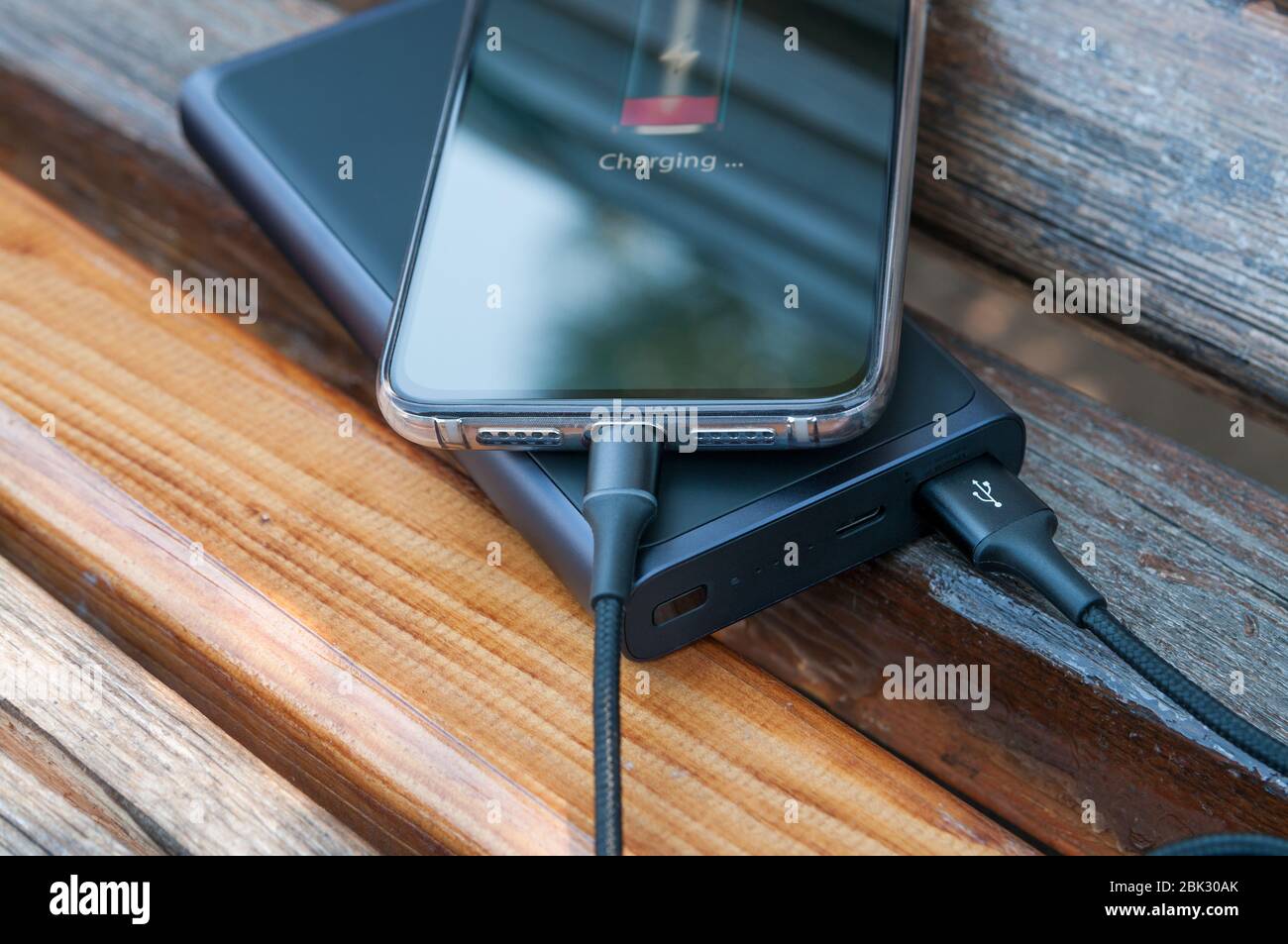 Il moderno smartphone si ricarica dal power bank su sfondo di legno. Concetto tecnologico moderno. Messa a fuoco selettiva. Foto Stock