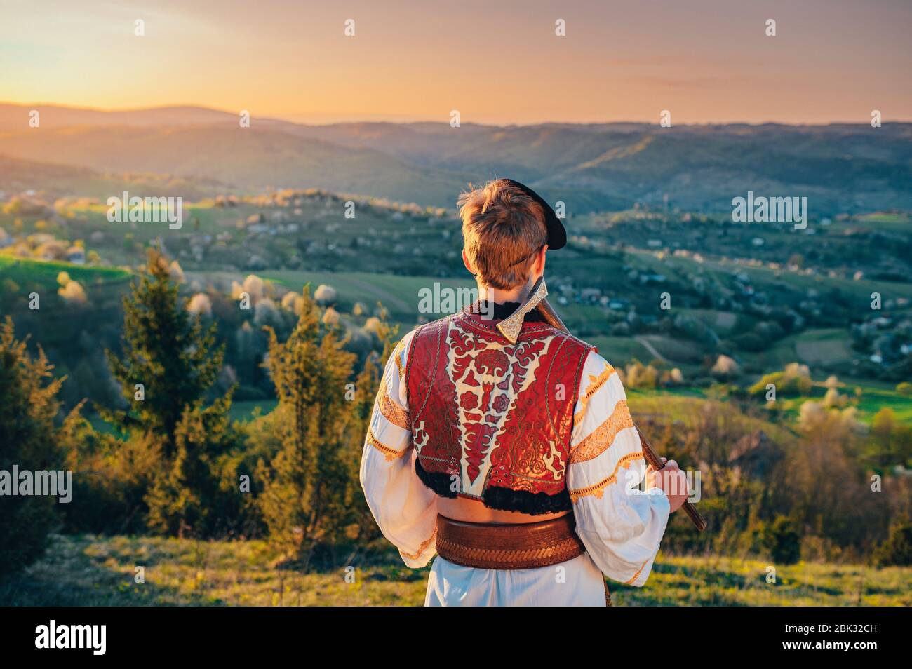 Giovane uomo in costume folk in piedi nella natura primaverile all'alba. Modifica spazio. Foto Stock