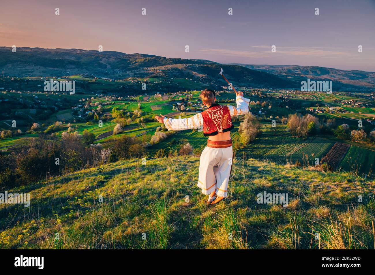 Un giovane in costume popolare slovacco guarda il paesaggio primaverile nel villaggio di Hrinova in Slovacchia. Sole che sorge e alberi in fiore primavera nel Foto Stock
