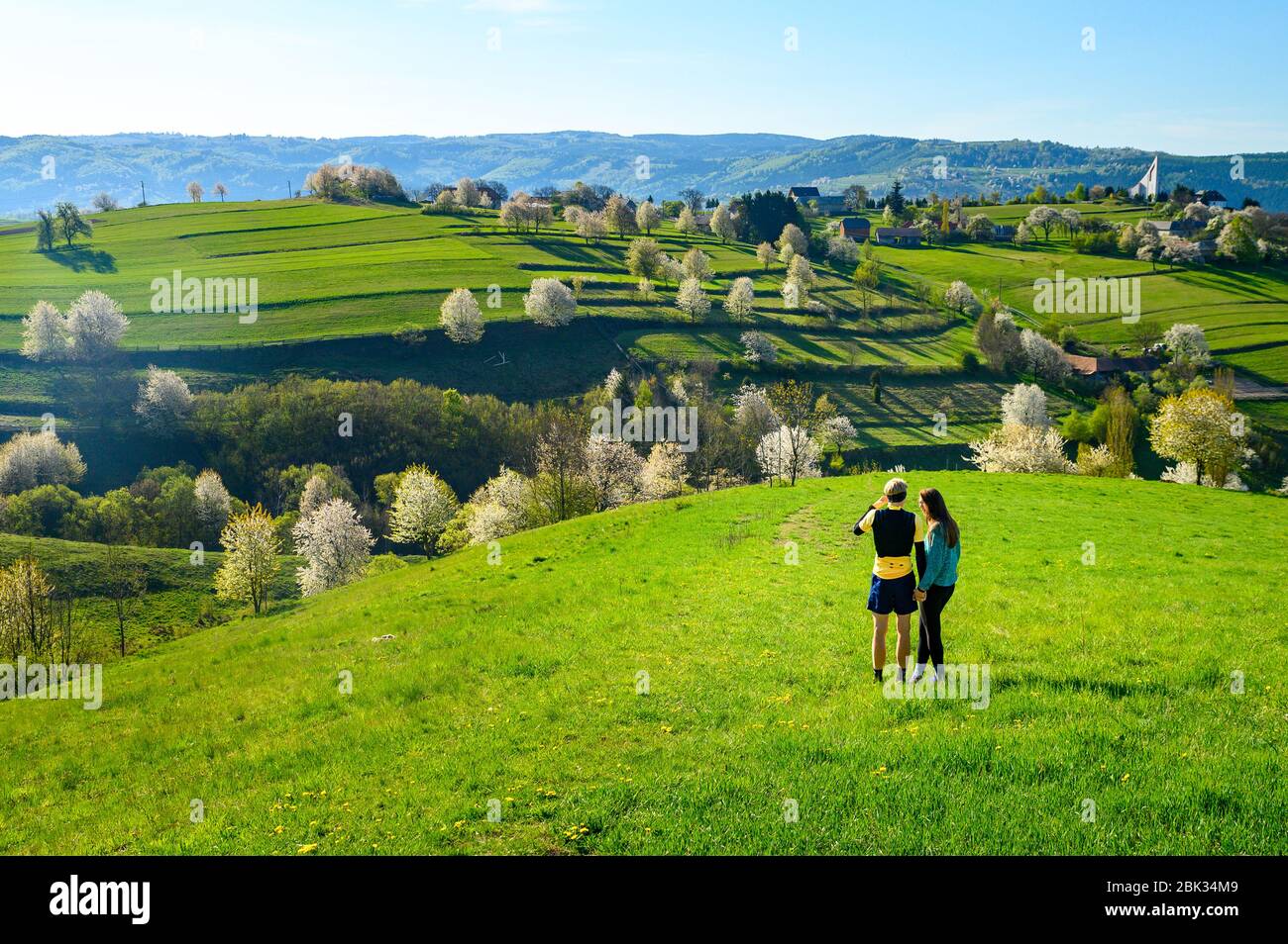 Giovane coppia innamorata verde primavera paesaggio, prati, alberi di ciliegio in fiore e bella vista Foto Stock