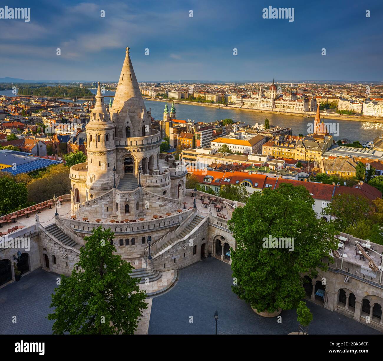 Budapest, Ungheria - veduta aerea del famoso Bastione dei pescatori al tramonto con edificio del Parlamento sullo sfondo. Luce solare calda, cielo blu, nessuna gente Foto Stock