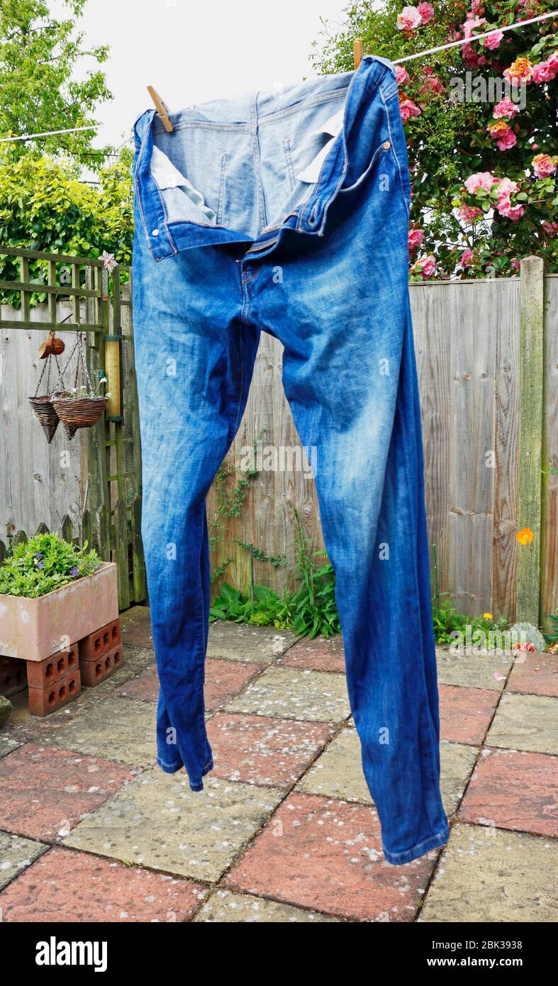 Un paio di jeans blu appeso a asciugare su una linea di lavaggio in un piccolo cortile residenziale pavimentato. Foto Stock