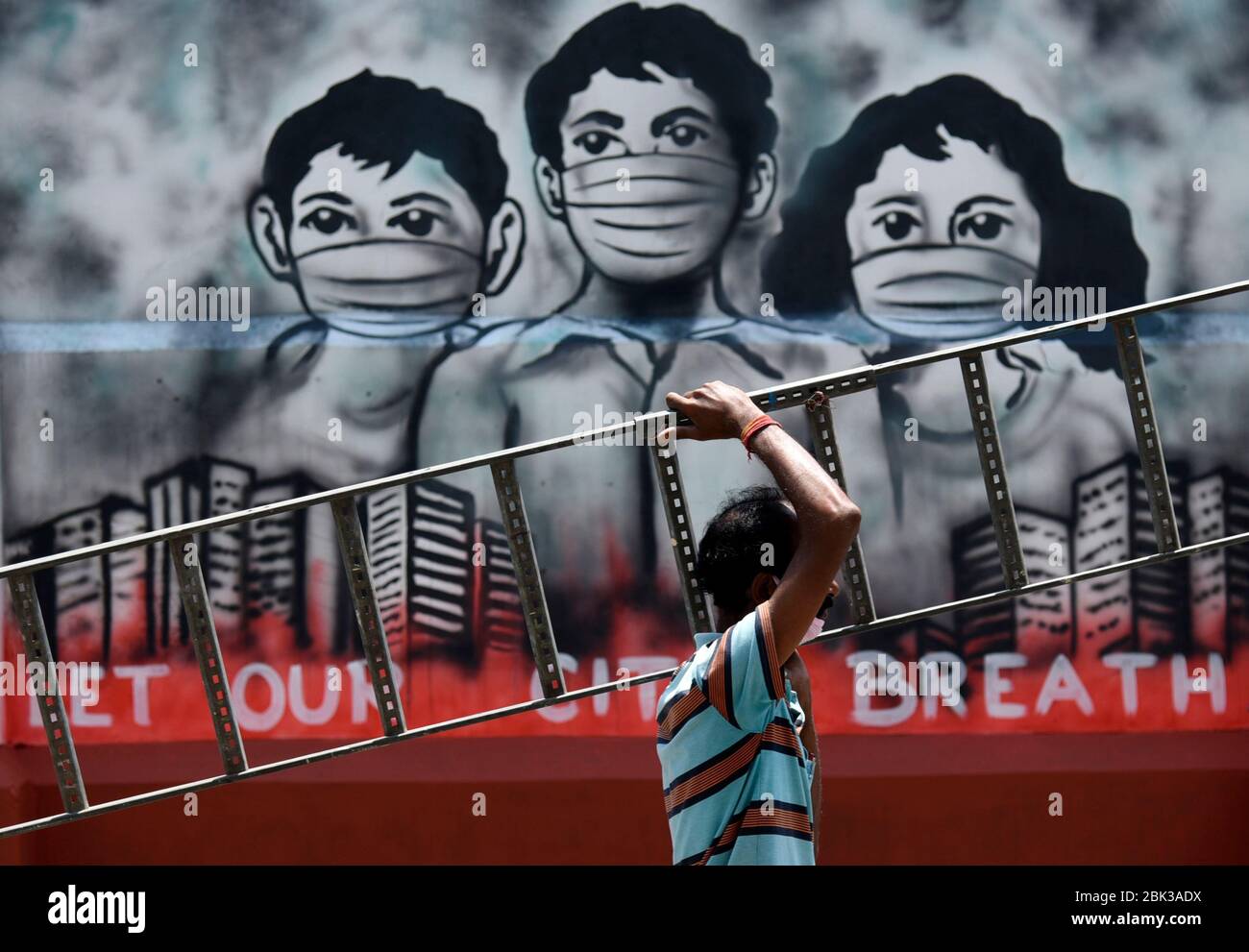 Guwahati, Assam, India. 1° maggio 2020. Un lavoro porta una scala che cammina oltre un mural correlato a coronavirus, durante l'arenamento a livello nazionale sulla scia della pandemia di coronavirus, a Guwahati. Credit: David Talukdar/ZUMA Wire/Alamy Live News Foto Stock