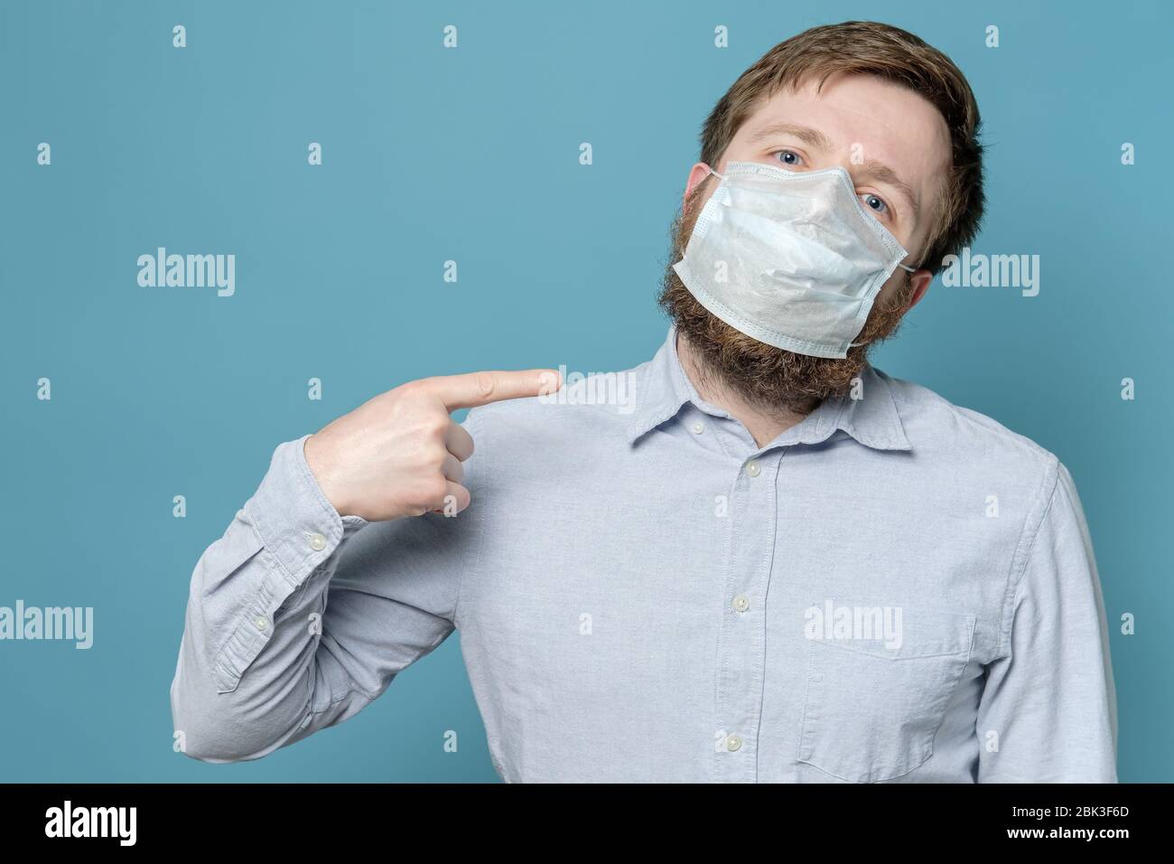 L'uomo punta il dito indice alla maschera medica sul suo viso, che non è aderente a causa della barba agile. Concetto di quarantena. Foto Stock