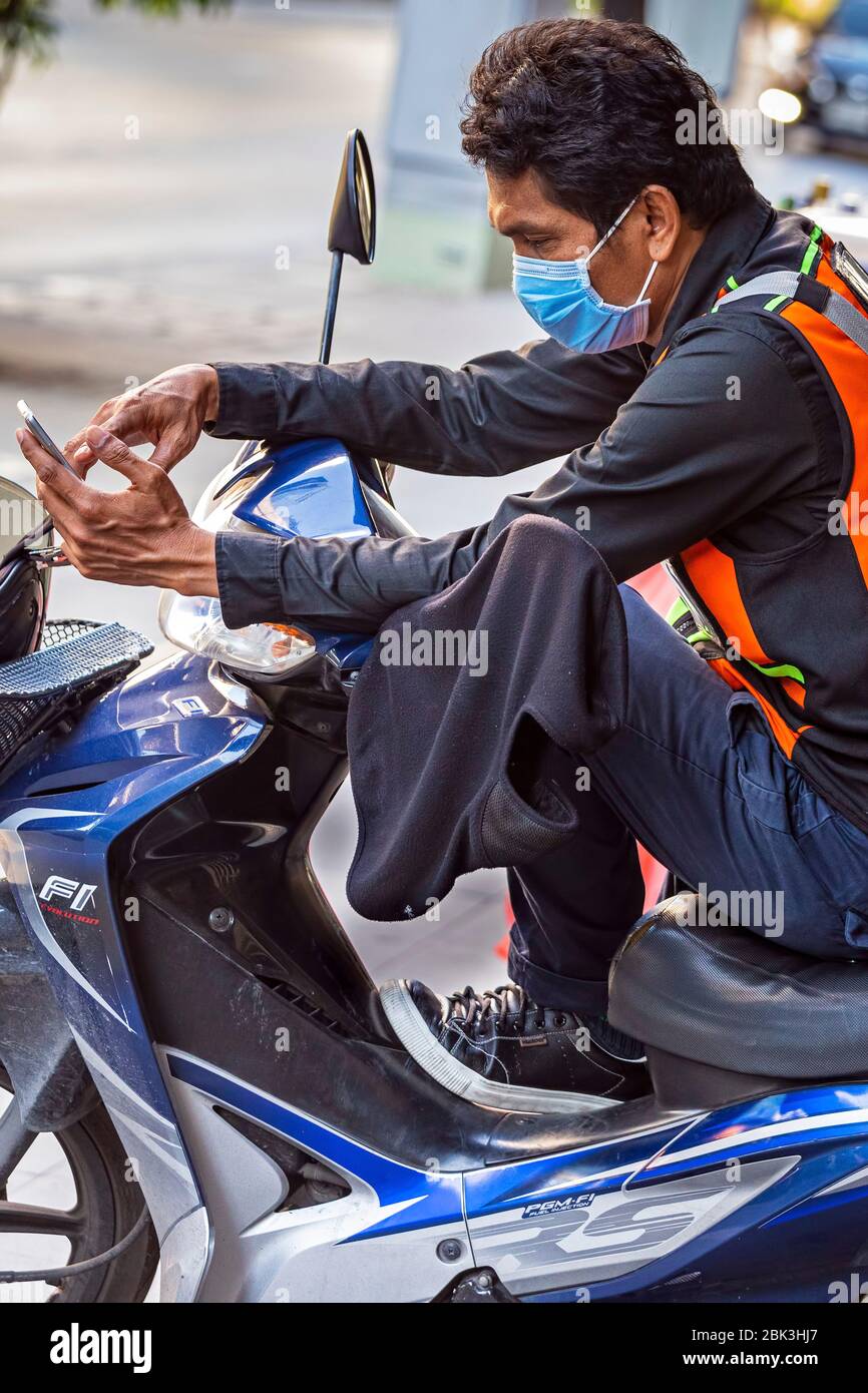 Tassista thailandese con maschera e telefono cellulare durante la pandemia Covid 19, Bangkok, Thailandia Foto Stock