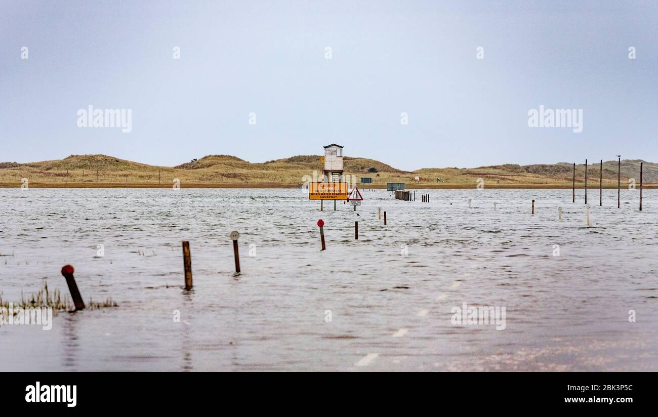 La strada alberata sull'isola di Lindisfarne con la scatola del rifugio di emergenza e i segnalatori stradali, Northumberland, Inghilterra Foto Stock