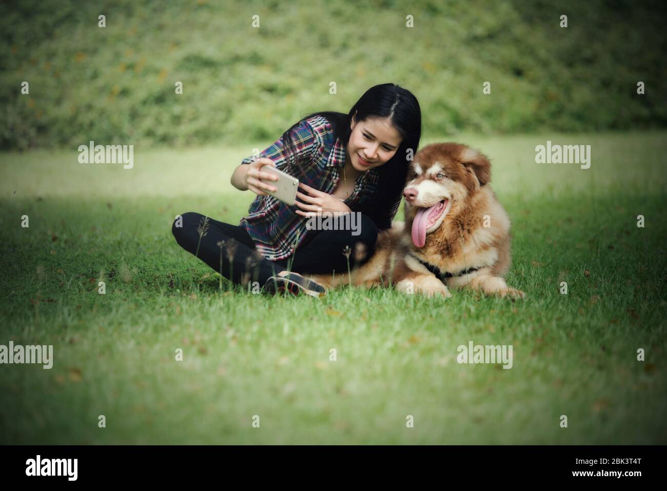 Bella giovane donna catturare foto con il suo piccolo cane in un parco all'aperto. Ritratto di stile di vita. Foto Stock