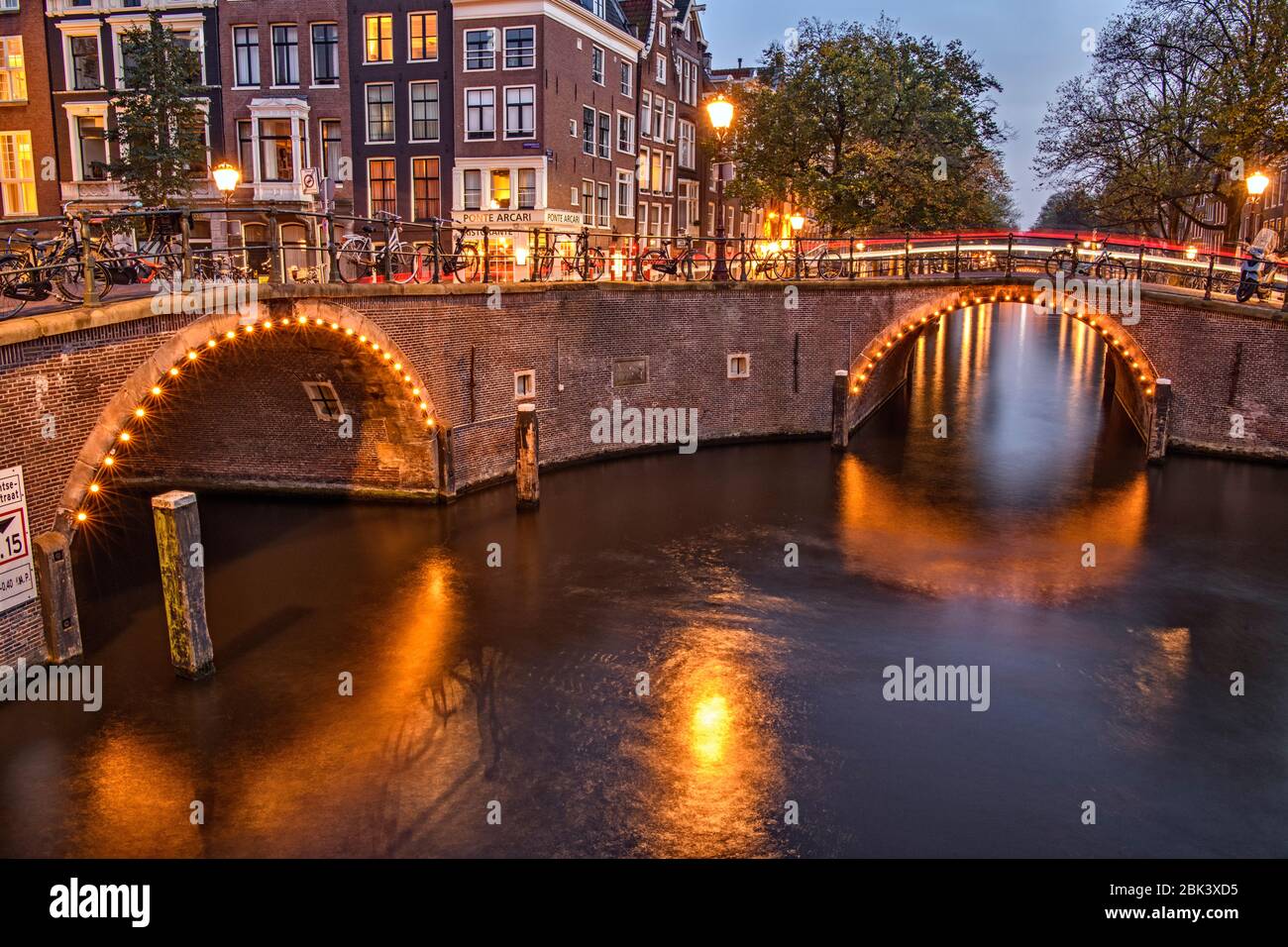 Riflessioni di luci a ponte nei canali al tramonto, Amsterdam, Olanda del Nord, Olanda Foto Stock