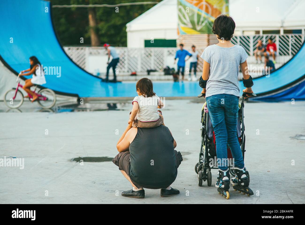 Mosca, Russia - 9 AGOSTO 2014: La giovane donna sportiva mamma guida uno skateboard nel parco Sokolniki mentre suo marito tiene un bambino sul collo Foto Stock