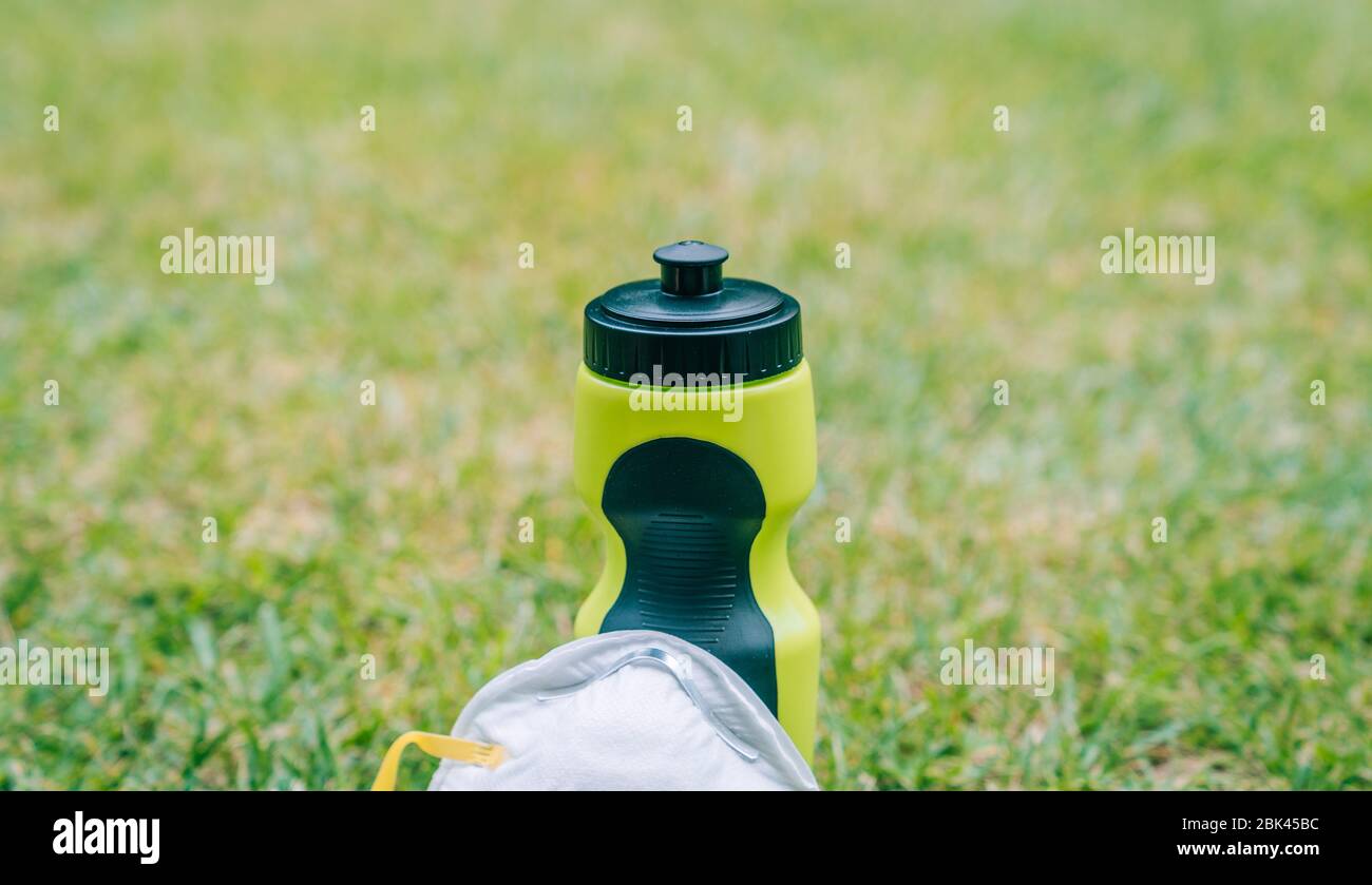 Bottiglia d'acqua per lo sport con maschera per andare all'aperto. Praticare sport nel parco adottando misure protettive per prevenire il coronavirus. Foto Stock