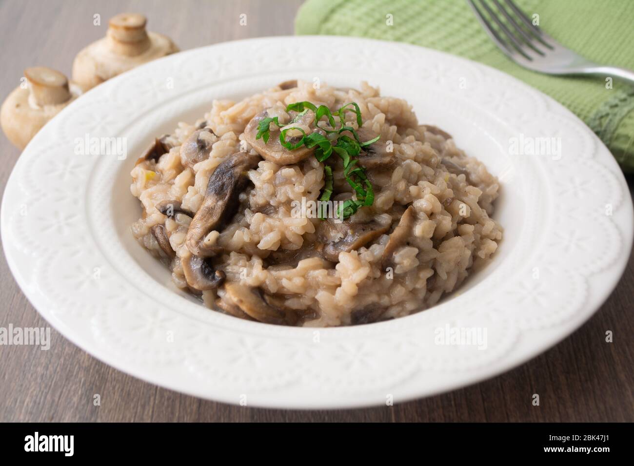 Risotto classico di funghi vegani a base di riso arborio, funghi, cipolla e aglio guarniti con nastri di basilico su una superficie rustica in legno Foto Stock