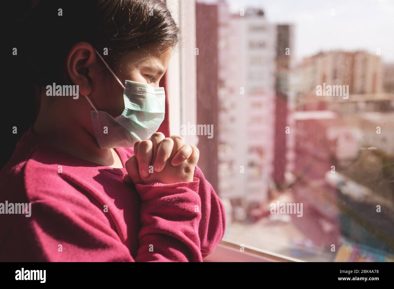 Bambina con maschera che prega per il passaggio del coronavirus Covid-19. Bambina prega di mano per Dio. Foto Stock