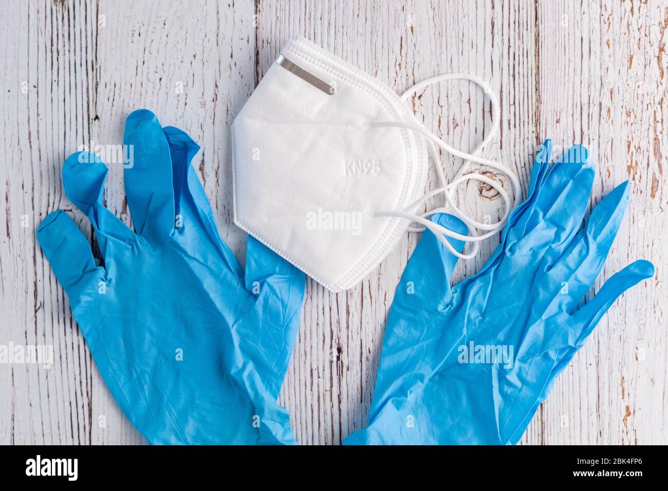 Maschera protettiva commerciale bianca KN95 e guanti in nitrile blu su sfondo bianco rustico Foto Stock