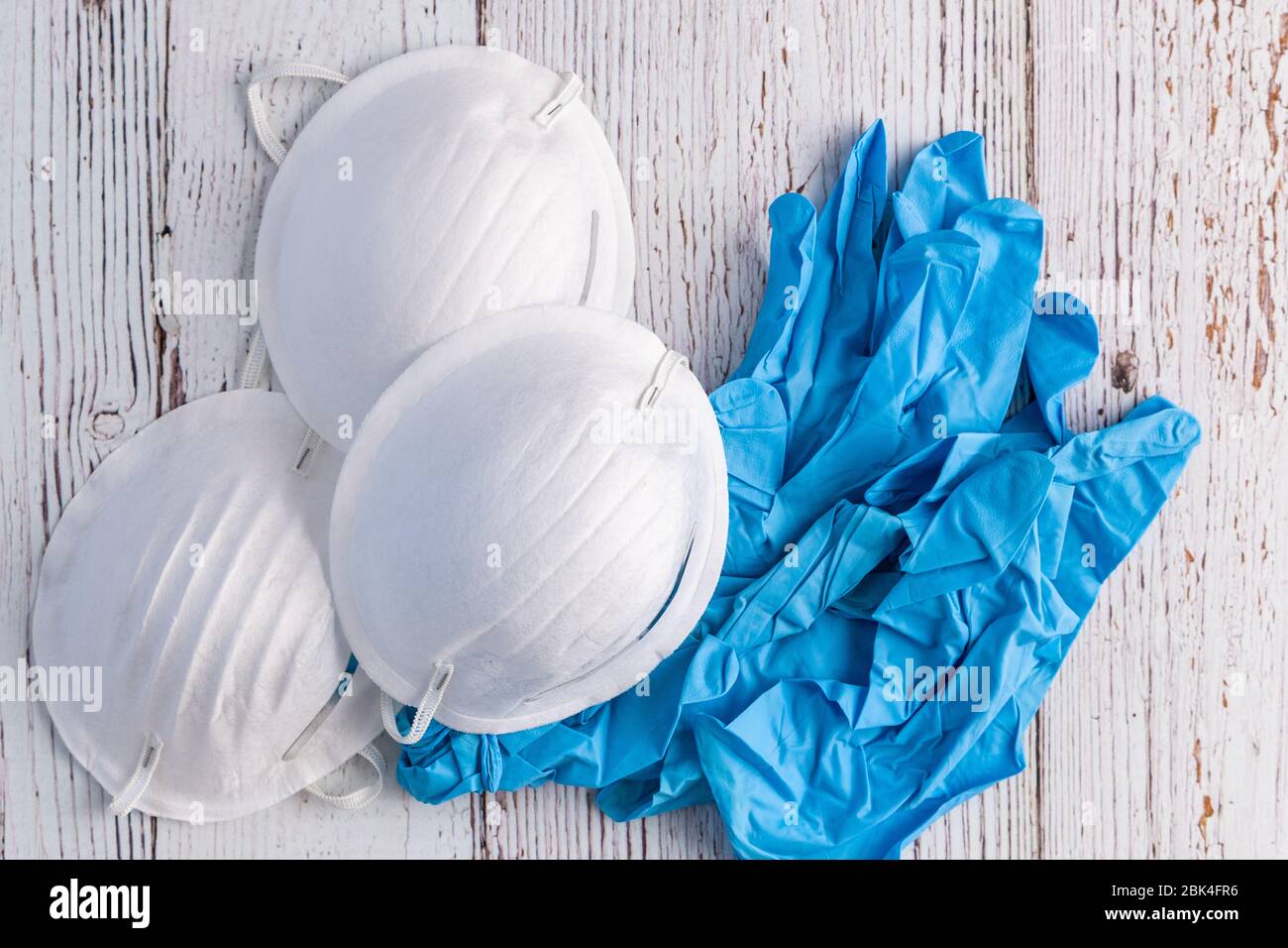 Maschere facciali di protezione commerciali bianche e guanti in nitrile blu su sfondo bianco rustico Foto Stock