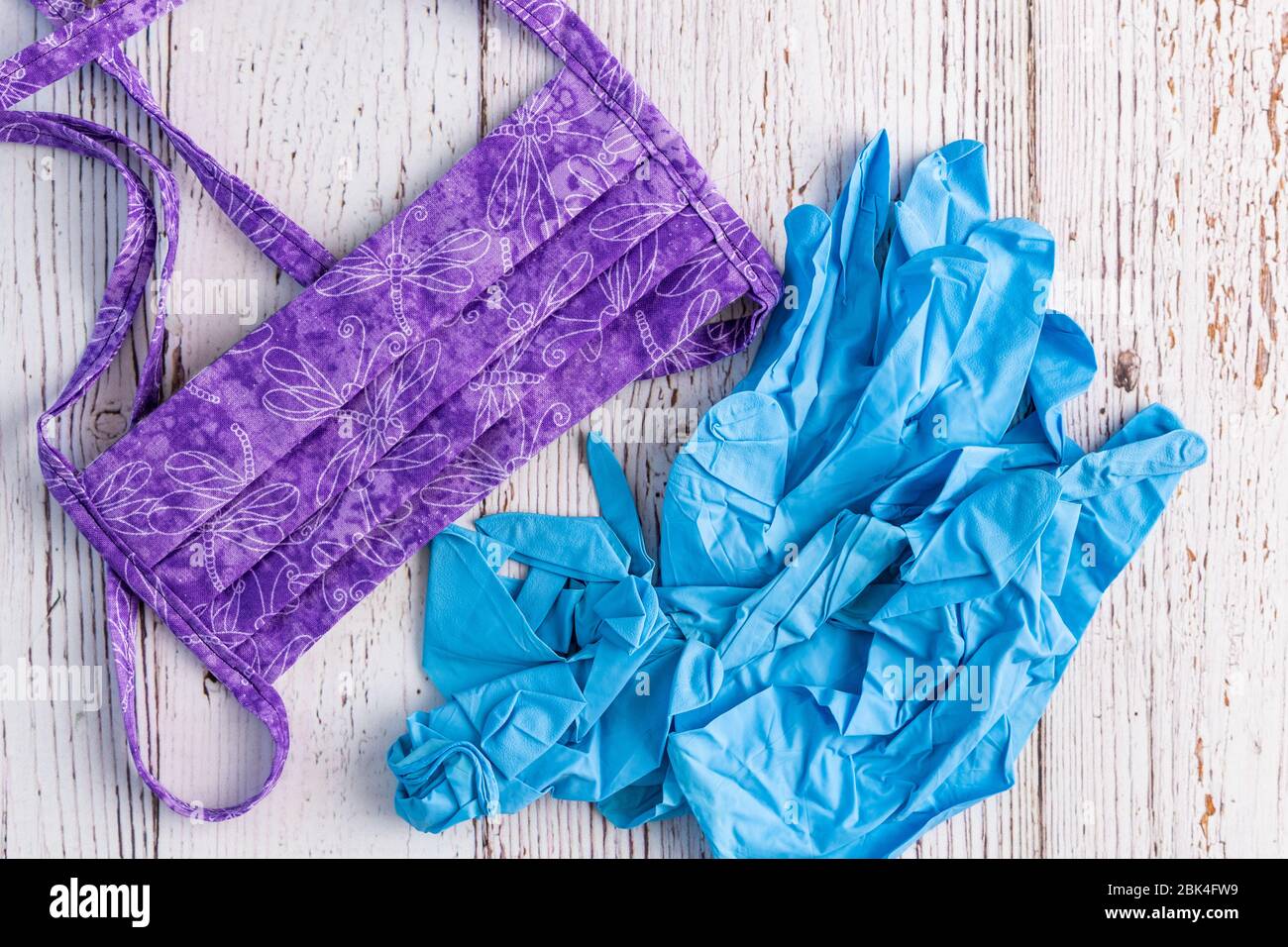 Maschera protettiva in tessuto viola fatta a mano e guanti in nitrile blu su fondo bianco rustico Foto Stock