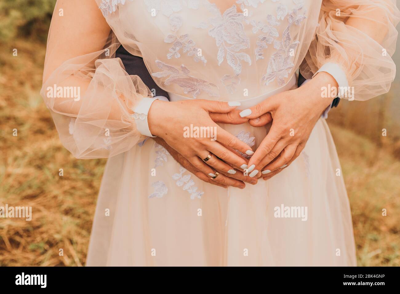 Due sposi che tengono le mani su un pancino a forma di cuore. Giorno del matrimonio. Foto Stock