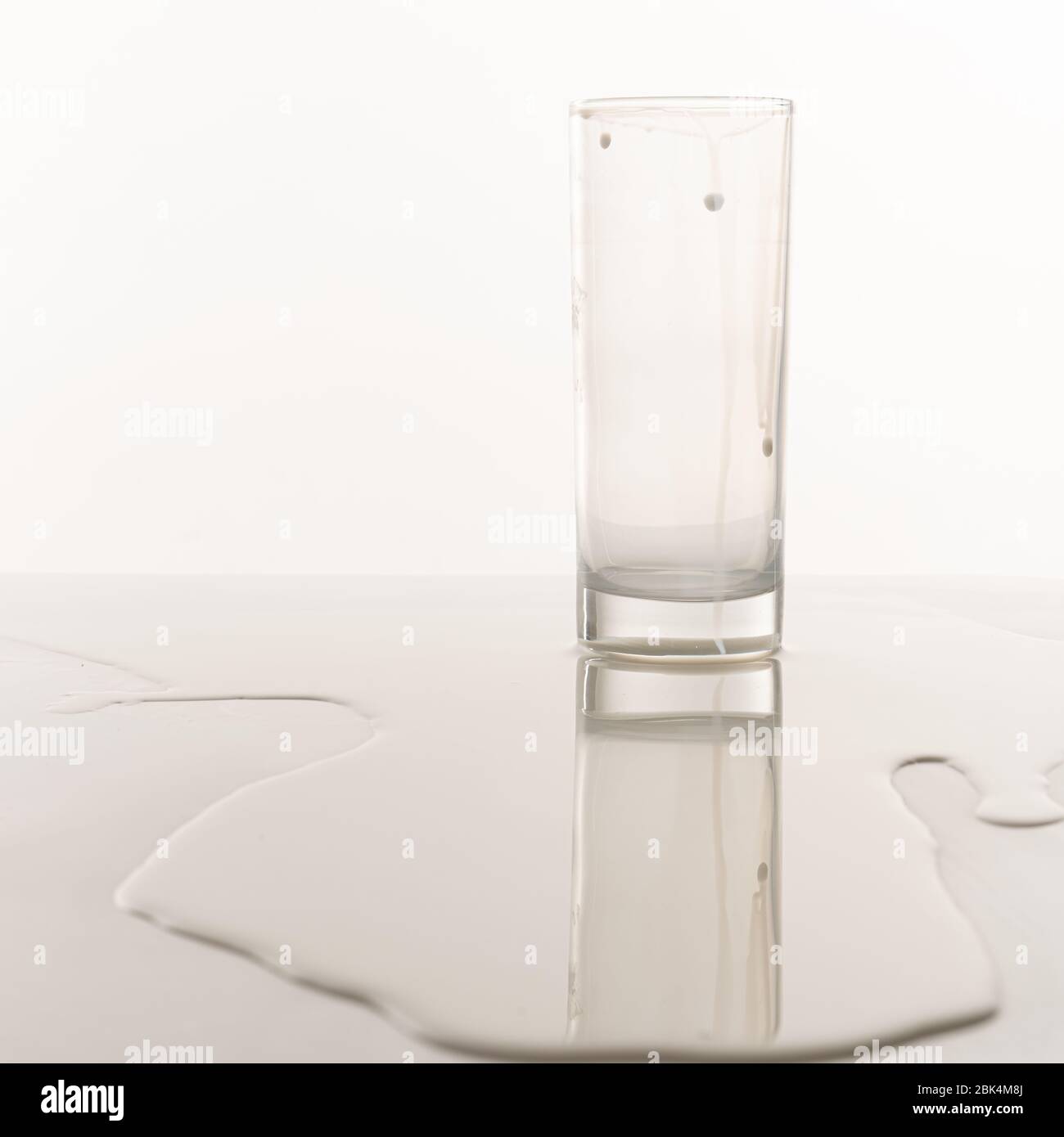 Il vetro vuoto si trova tra il latte versato sul tavolo Foto Stock