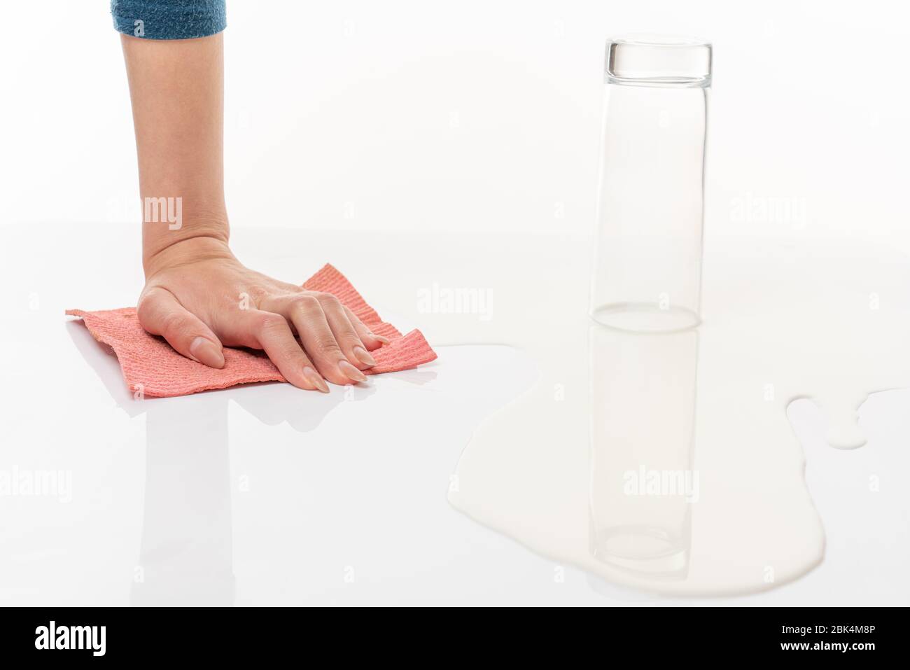 Bicchiere vuoto rovesciato tra il latte versato e la mano femminile con straccio Foto Stock