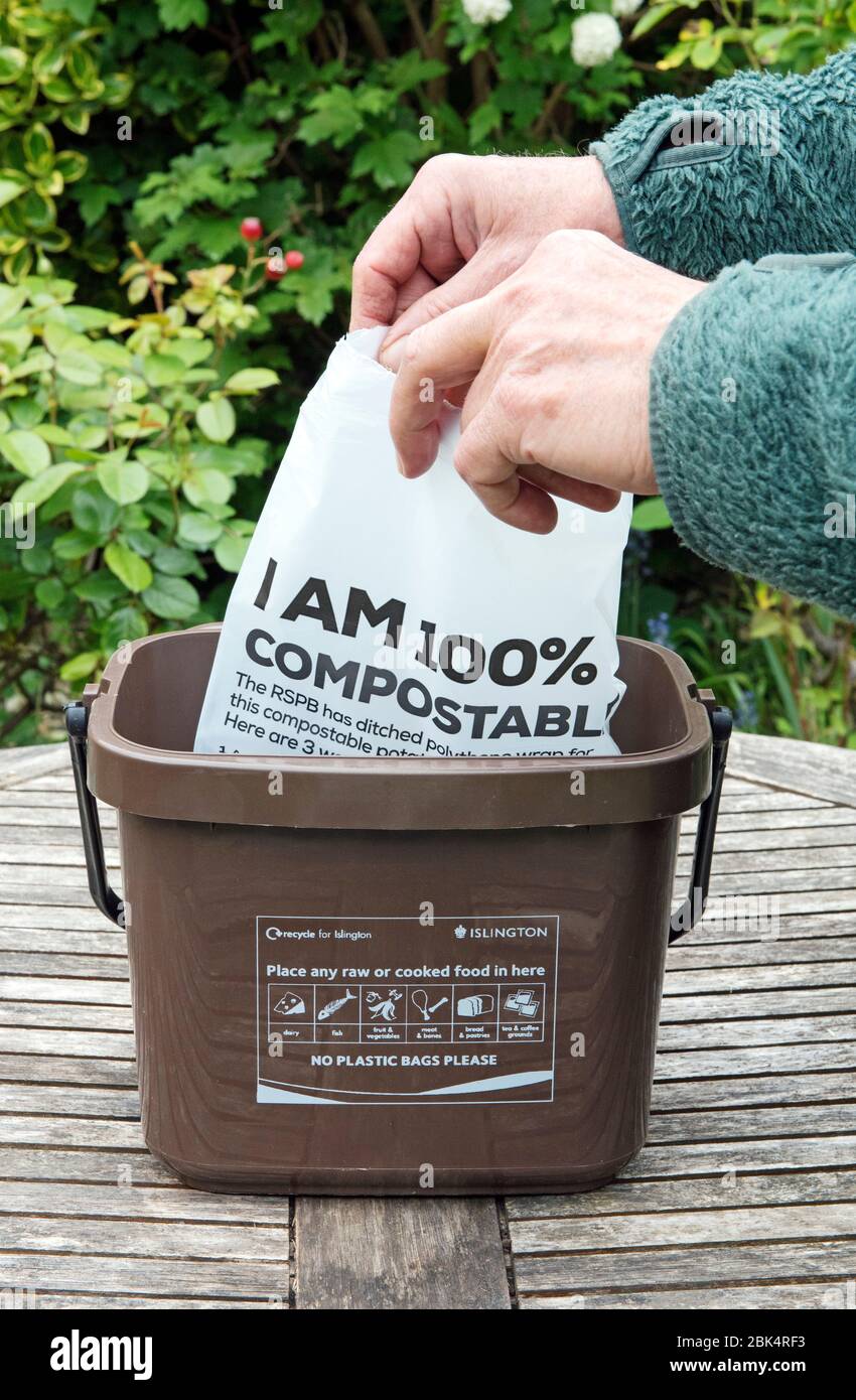 Uomo rivestimento composto bin con compostable rivista imballaggio o imballaggio dicendo 'sono 100% compostable' su tavolo da giardino. Foto Stock