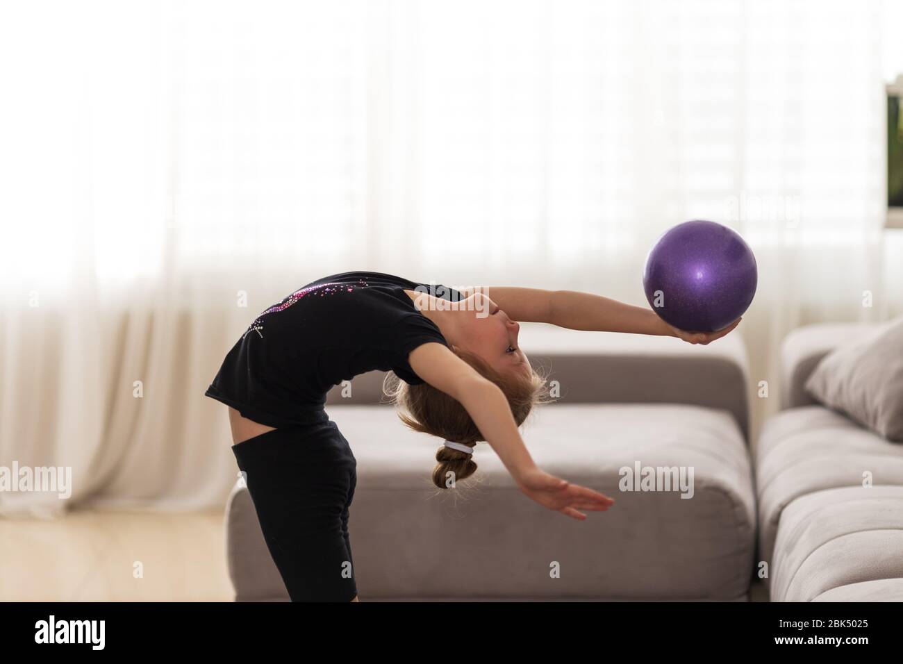 La piccola ragazza ginnastica esegue varie ginnastica e esercizi di fitness a casa. Il concetto di infanzia e sport Foto Stock