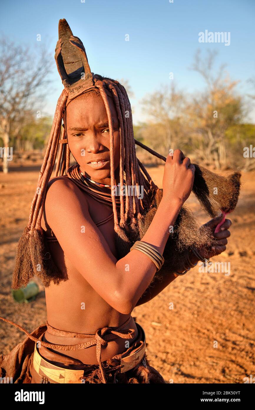 Batwa ragazza in abito tradizionale pettinando i capelli al tramonto. Foto Stock