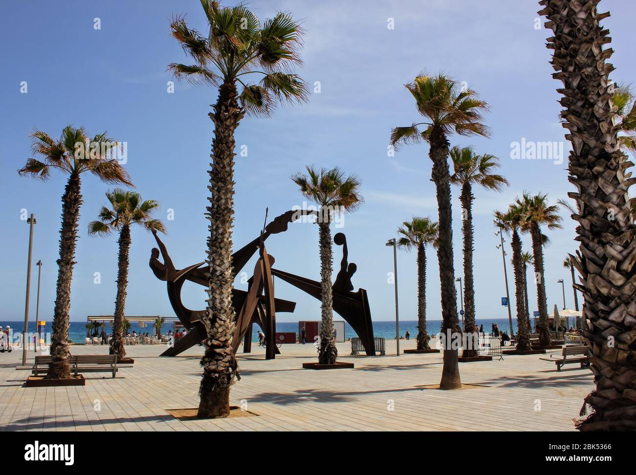 Una vista sulla spiaggia di Barceloneta, la spiaggia più popolare di Barcellona, Catalogna, Spagna. La scultura olimpica tra le palme viste in lontananza. Foto Stock