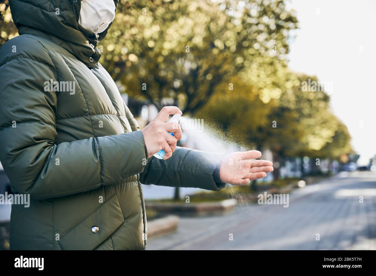 Immagine ravvicinata delle mani della donna in maschera, in strada, strofinandole mani con spray lavante mani come misura igienica preventiva contro l'infezione da Covid-19. Mantenere la distanza sociale Foto Stock