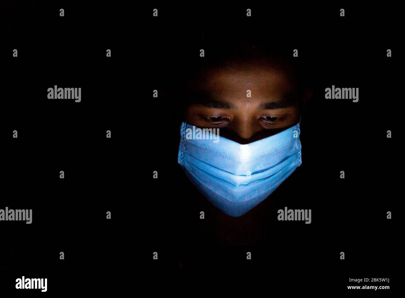 Un giovane uomo blu con maschera chirurgica stava giocando a giochi per smartphone a Dhaka. Foto Stock