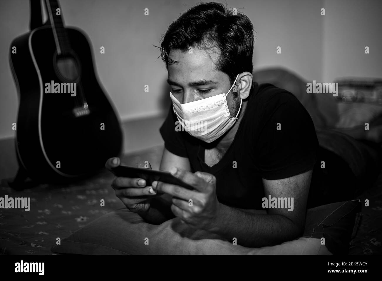 Un giovane uomo con maschera chirurgica stava giocando a giochi mobili a casa sua a causa della quarantena domestica del coronavirus a Dhaka. Foto Stock