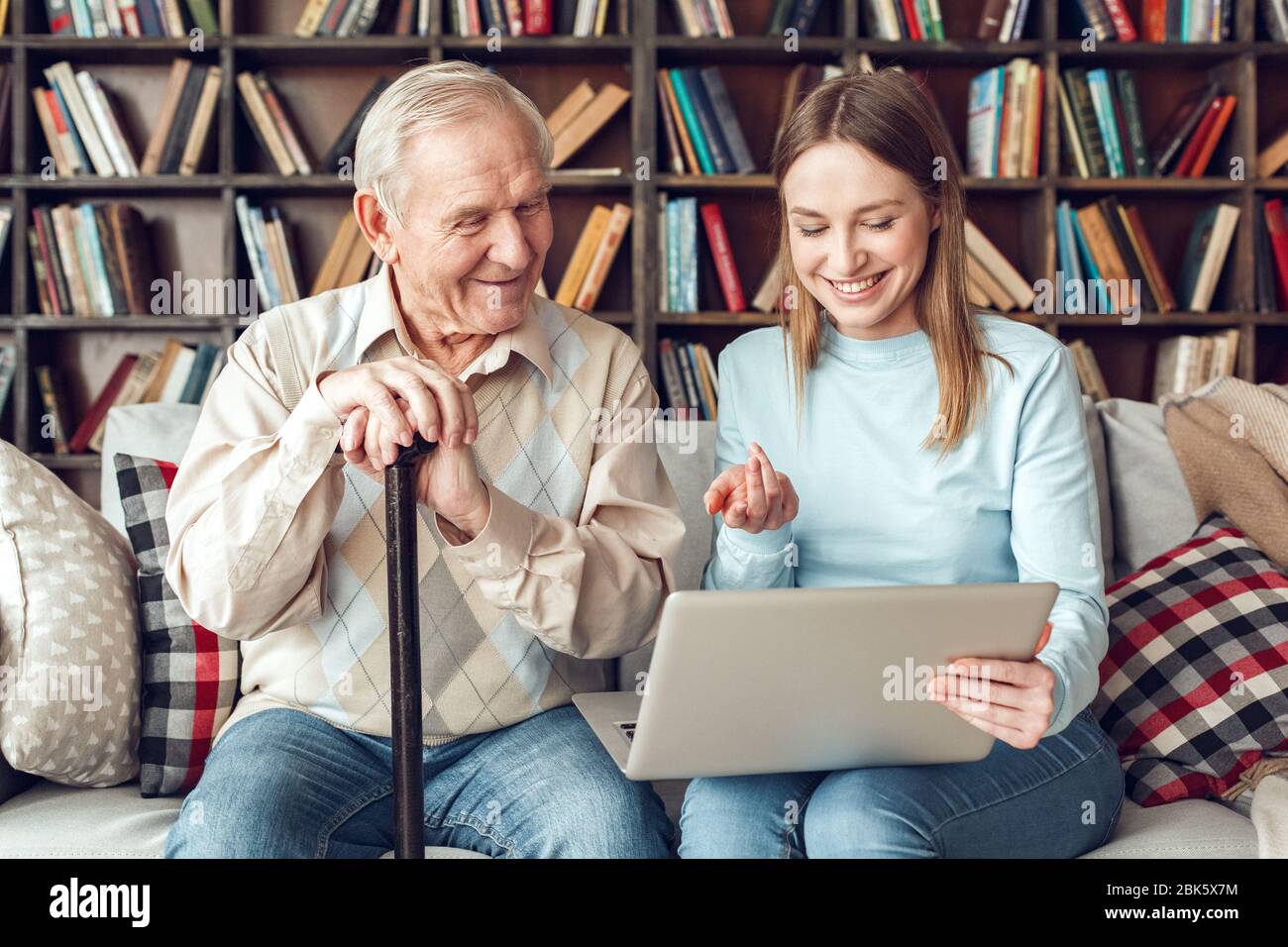 Padre e figlia a casa libreria seduto guardando il notebook sorridente Foto Stock